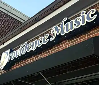 Storefront sign reading Providence Music mounted on a brick building exterior